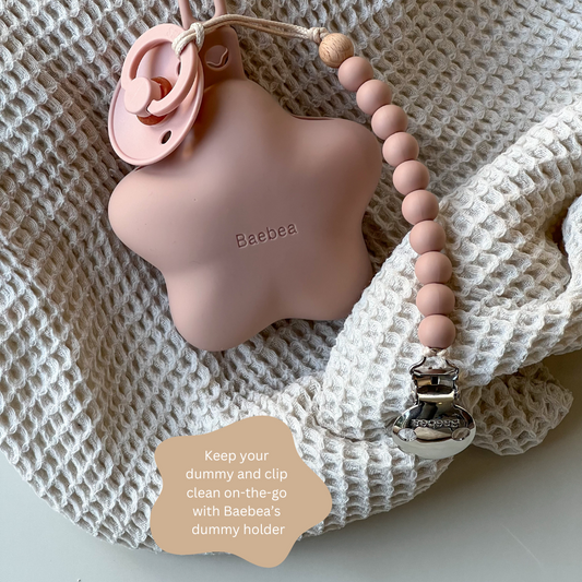 A personalised dummy clip and holder set in a soothing muted color, with a star-shaped clip and a round holder, displayed on a textured white surface. The brand 'Baebea' is visible on the clip, and the image includes a note suggesting to keep the dummy clean and clip on the go.